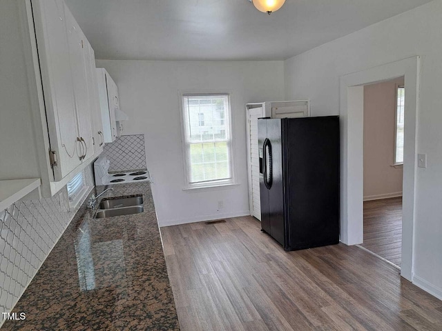 kitchen with light hardwood / wood-style flooring, black fridge with ice dispenser, sink, white cabinetry, and dark stone countertops