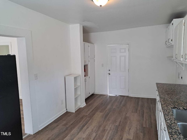 kitchen with dark stone countertops, white cabinetry, black fridge, and dark hardwood / wood-style flooring