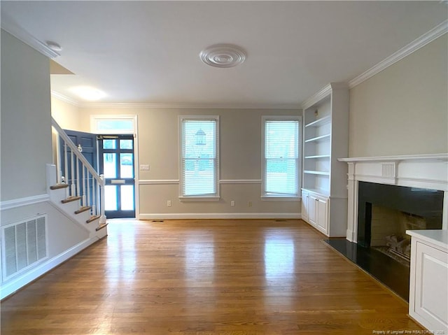 unfurnished living room featuring ornamental molding, hardwood / wood-style flooring, and built in shelves