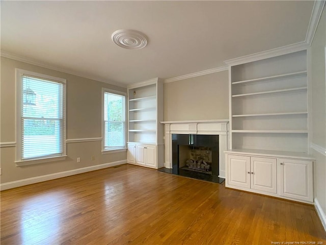 unfurnished living room featuring built in shelves, ornamental molding, and light hardwood / wood-style floors