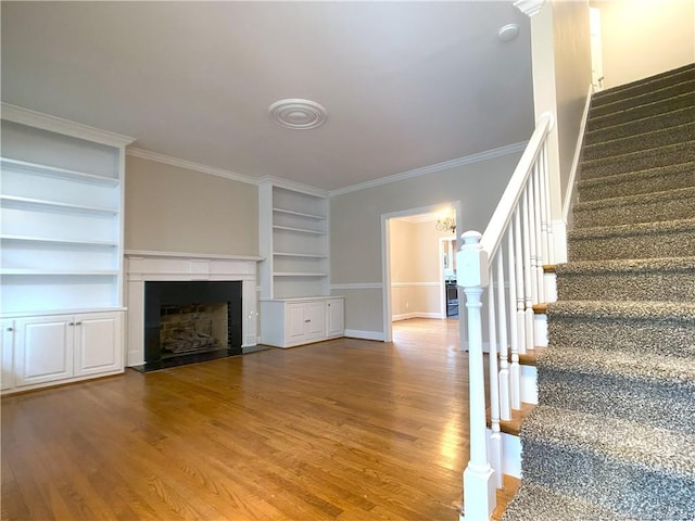 unfurnished living room featuring built in shelves, wood-type flooring, and crown molding