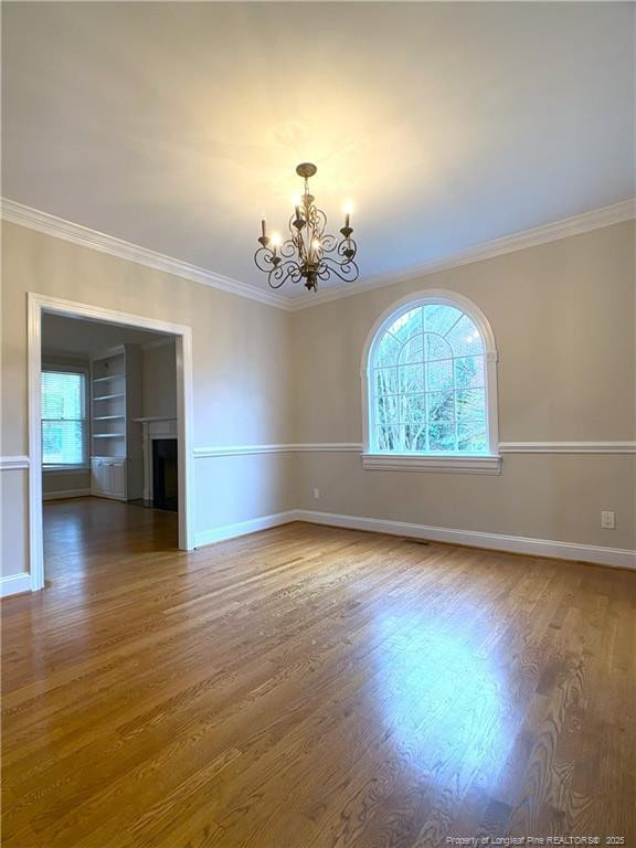 empty room featuring crown molding, built in features, dark hardwood / wood-style flooring, and an inviting chandelier