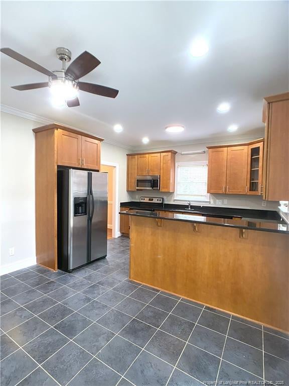 kitchen with kitchen peninsula, ceiling fan, appliances with stainless steel finishes, crown molding, and a breakfast bar