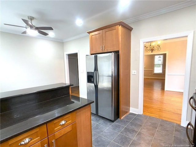 kitchen featuring stainless steel fridge, dark stone countertops, ceiling fan with notable chandelier, and ornamental molding