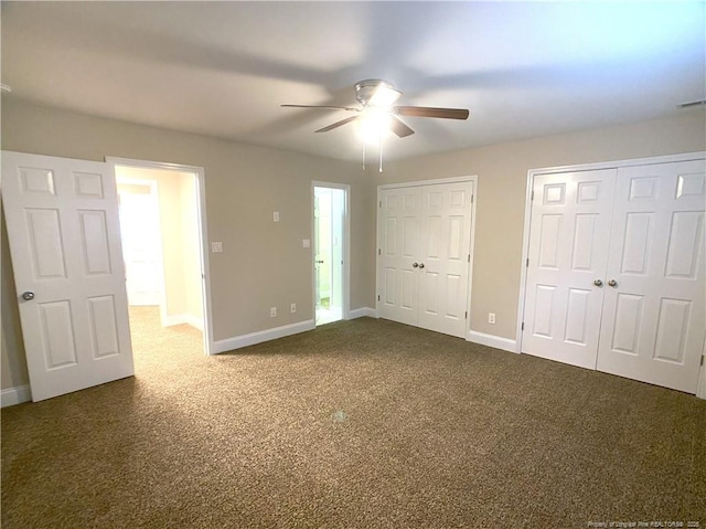 unfurnished bedroom with ceiling fan, dark colored carpet, and multiple closets