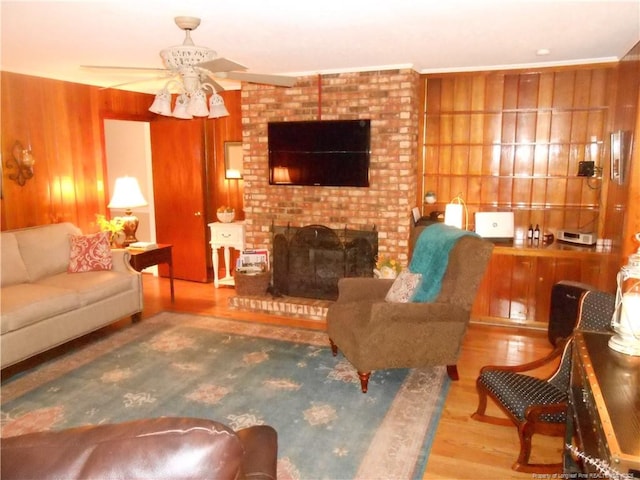 living room with ceiling fan, a brick fireplace, hardwood / wood-style floors, and wooden walls