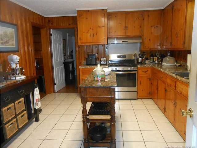 kitchen featuring gas stove, ornamental molding, light tile patterned floors, and wooden walls