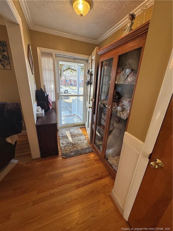 doorway to outside with hardwood / wood-style floors, ornamental molding, and a textured ceiling