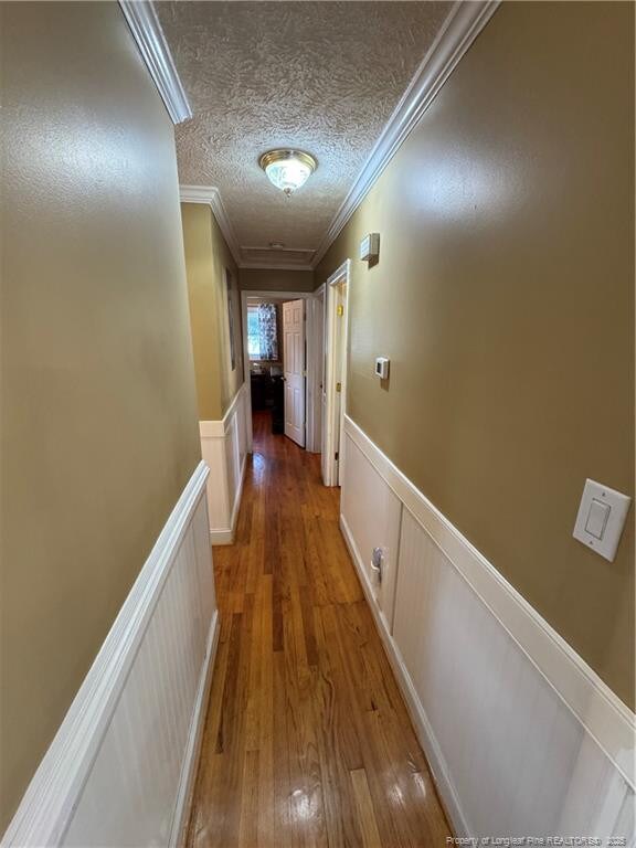 hallway featuring a textured ceiling, ornamental molding, and wood-type flooring