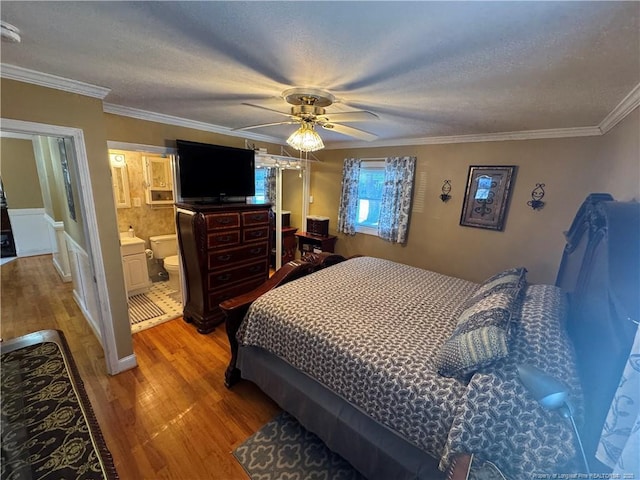 bedroom with ceiling fan, hardwood / wood-style floors, a textured ceiling, connected bathroom, and ornamental molding