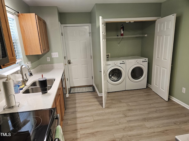 clothes washing area featuring light hardwood / wood-style floors, washer and clothes dryer, and sink