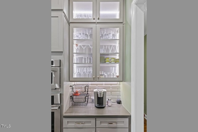 bar with gray cabinets, stainless steel oven, and backsplash