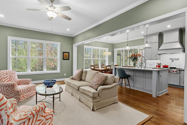 living room featuring hardwood / wood-style flooring, ceiling fan, ornamental molding, and plenty of natural light