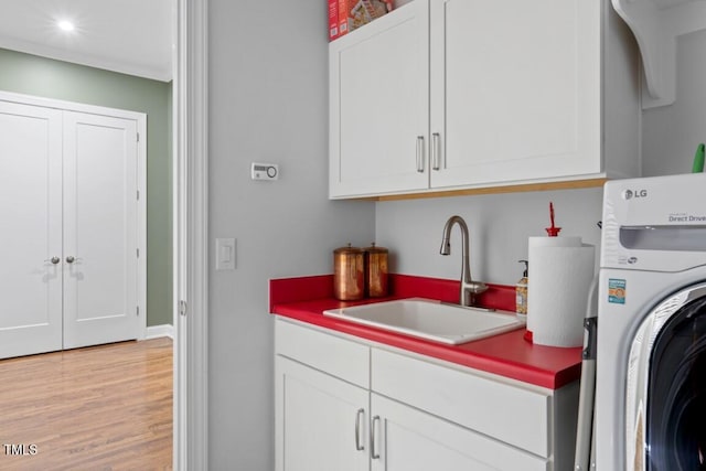 clothes washing area with washer / clothes dryer, light hardwood / wood-style flooring, cabinets, and sink