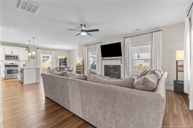 living room featuring sink, ceiling fan with notable chandelier, plenty of natural light, and light wood-type flooring