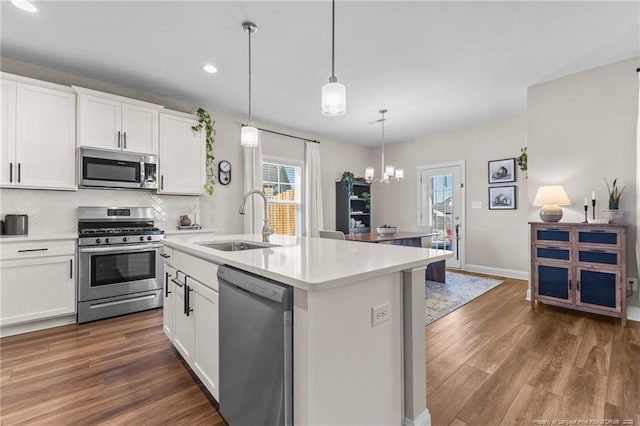 kitchen with sink, hanging light fixtures, appliances with stainless steel finishes, a kitchen island with sink, and white cabinets