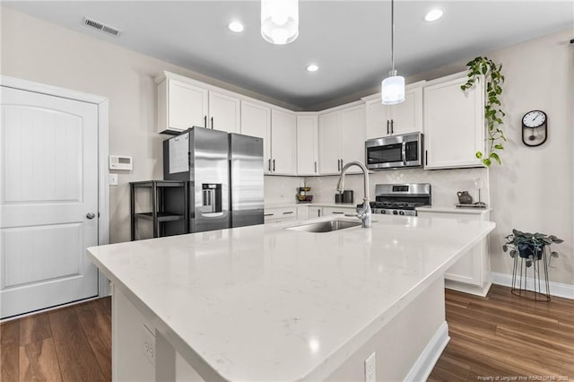 kitchen featuring pendant lighting, an island with sink, white cabinets, stainless steel appliances, and light stone countertops