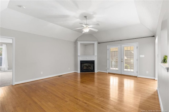 unfurnished living room with light wood-type flooring, a wealth of natural light, vaulted ceiling, and french doors