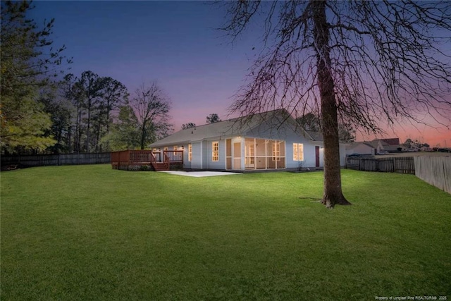 back house at dusk featuring a lawn, a deck, and a patio