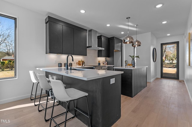 808 Culpepper Ln, Raleigh, NC 27610 - kitchen with pendant lighting, sink, light hardwood / wood-style floors, a center island with sink, and wall chimney exhaust hood