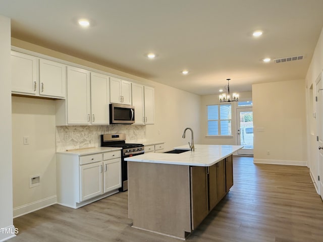 kitchen featuring stainless steel appliances, tasteful backsplash, light wood-style flooring, white cabinets, and a sink