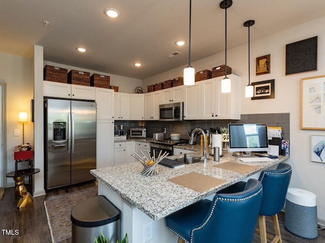 kitchen featuring appliances with stainless steel finishes, a peninsula, dark wood finished floors, white cabinets, and light stone counters