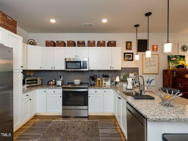 kitchen featuring appliances with stainless steel finishes, a sink, a peninsula, dark wood-type flooring, and white cabinetry