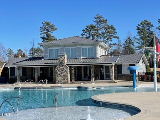 exterior space featuring a patio area, stone siding, metal roof, and a community pool