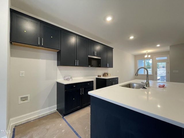 kitchen with dark cabinets, light countertops, decorative backsplash, and a sink