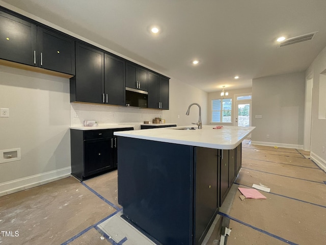 kitchen with visible vents, baseboards, dark cabinets, a center island with sink, and a sink