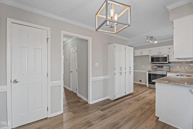 kitchen with pendant lighting, sink, crown molding, stainless steel appliances, and white cabinets