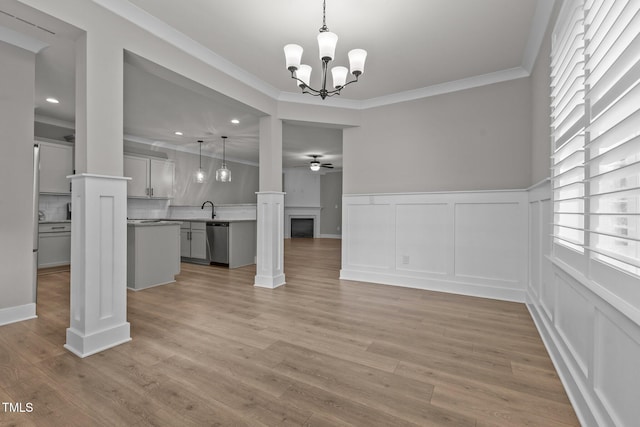 unfurnished living room with ceiling fan with notable chandelier, ornate columns, light hardwood / wood-style floors, sink, and ornamental molding