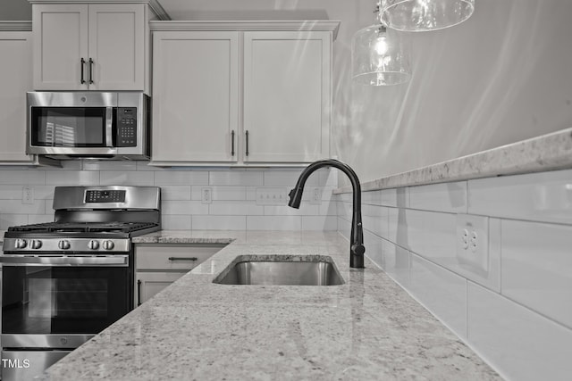 kitchen with white cabinets, stainless steel appliances, sink, backsplash, and light stone counters