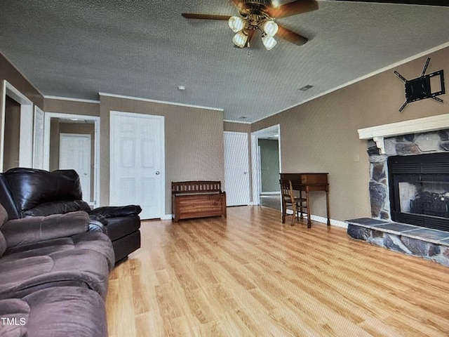 living area featuring a textured ceiling, ceiling fan, a fireplace, wood finished floors, and crown molding