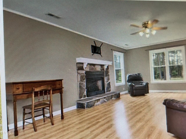 living room with a ceiling fan, a stone fireplace, wood finished floors, baseboards, and wallpapered walls