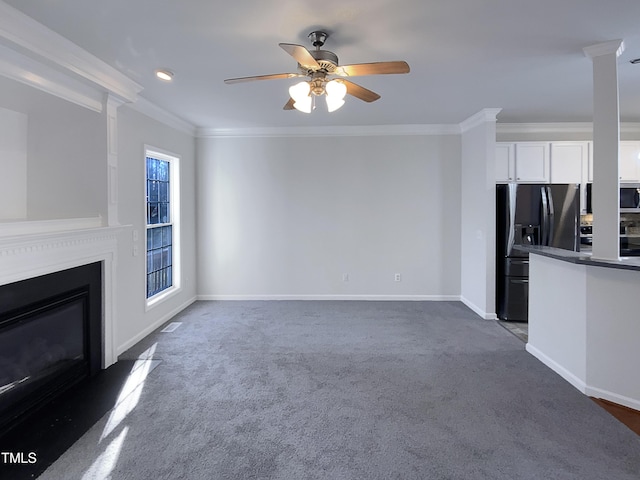 unfurnished living room featuring ceiling fan, crown molding, ornate columns, and dark colored carpet