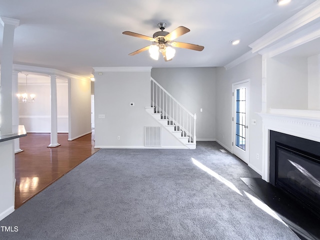 unfurnished living room with ornate columns, ornamental molding, ceiling fan with notable chandelier, and dark carpet