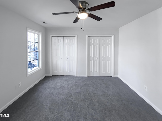 unfurnished bedroom with ceiling fan, two closets, and dark colored carpet