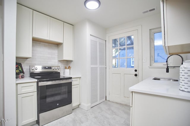 kitchen with tasteful backsplash, sink, a healthy amount of sunlight, stainless steel range with electric stovetop, and white cabinets