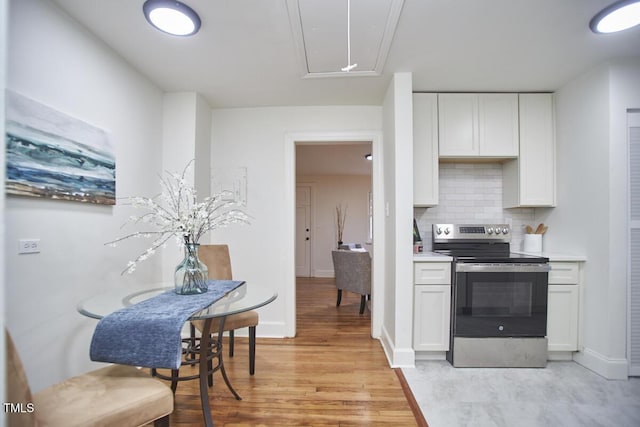 kitchen with stainless steel electric range oven, backsplash, white cabinetry, and light hardwood / wood-style flooring