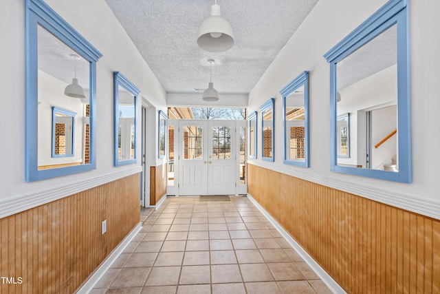 doorway to outside featuring french doors, wooden walls, a textured ceiling, and light tile patterned floors