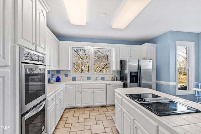 kitchen featuring appliances with stainless steel finishes, a wealth of natural light, sink, and white cabinets