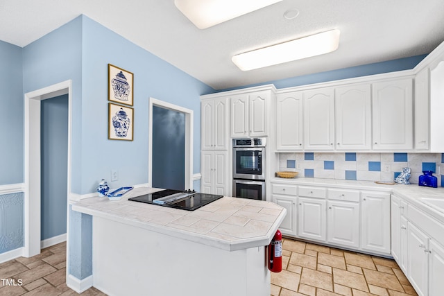 kitchen with white cabinetry, black electric cooktop, tile counters, double oven, and backsplash