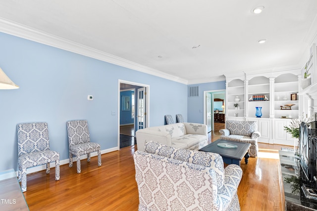 living room featuring built in shelves, ornamental molding, and light hardwood / wood-style floors