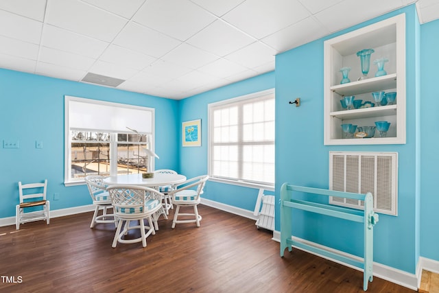 dining area with a drop ceiling, dark wood-type flooring, and built in features