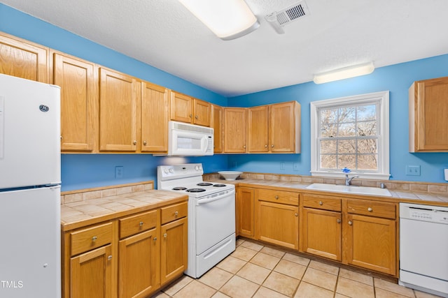 kitchen featuring sink, a textured ceiling, light tile patterned floors, tile counters, and white appliances