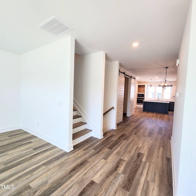 corridor with dark wood-type flooring, a barn door, and an inviting chandelier