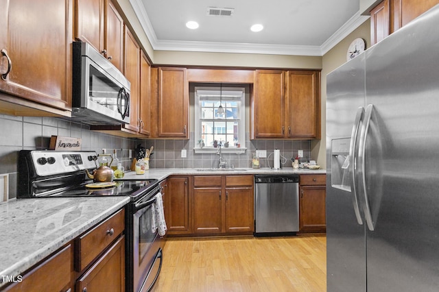 kitchen with tasteful backsplash, appliances with stainless steel finishes, sink, and light hardwood / wood-style floors