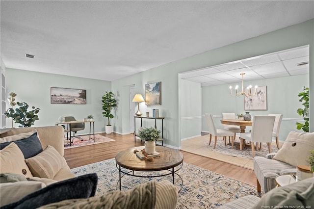 living area with a drop ceiling, light wood-style flooring, visible vents, baseboards, and an inviting chandelier