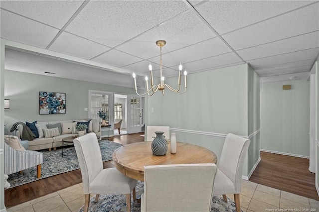 dining room with light tile patterned floors, a drop ceiling, baseboards, and a notable chandelier